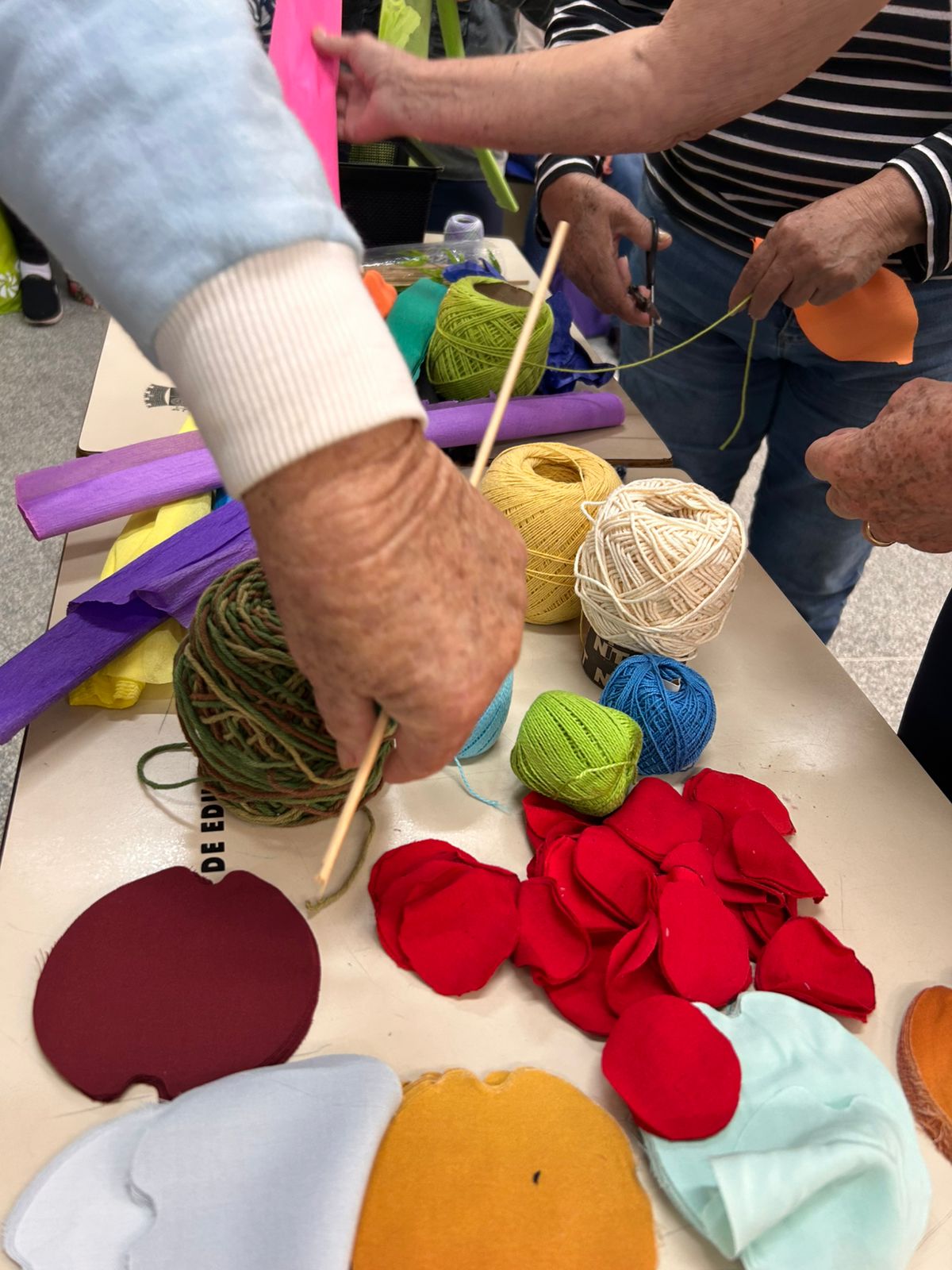 Mãos escolhendo linhas, tecidos e materiais coloridos em vivência arteterapêutica
